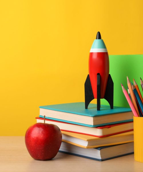 Bright toy rocket and school supplies on wooden table. Space for text