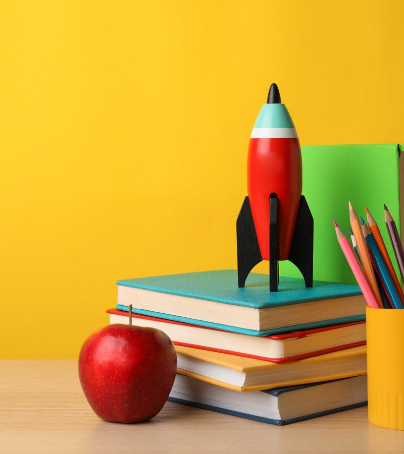 Bright toy rocket and school supplies on wooden table. Space for text