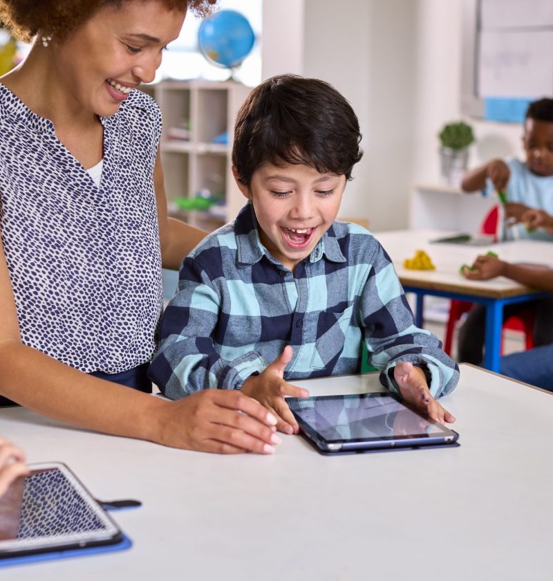 Female Teacher With Multi-Cultural Elementary School Pupils Using Digital Tablets At School